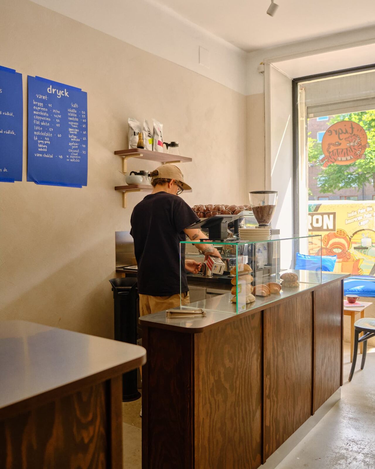 A barista in a black t-shirt and tan cap making coffee at Tigre Kaffebar